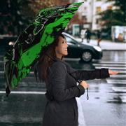 A woman in a dark gray coat stands on a rainy city street holding a large open umbrella. The umbrella has a bold black and neon green graphic design.