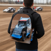 A man viewed from behind wearing a black backpack with a large printed graphic of a blue and white race car on a dirt track, with race cars visible in the background.