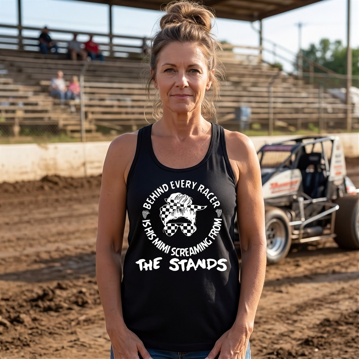 A woman standing on a dirt racetrack wearing a black tank top with a white graphic that reads 'BEHIND EVERY RACER KISSES MINI SCREAMING FROM THE STANDS' with a checkered horse illustration.