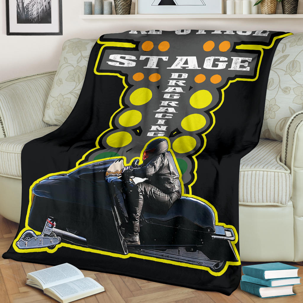 Black snowmobile asphalt blanket displayed across a cream sofa, featuring a sample rider photo, staging lettering, and yellow starting lights.