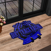 A rectangular doormat featuring a blue and black dirt track racing design with the words 'DIRT TRACK RACING', a checkered flag motif, and a stylized race car, placed on a wood floor in front of glass doors.
