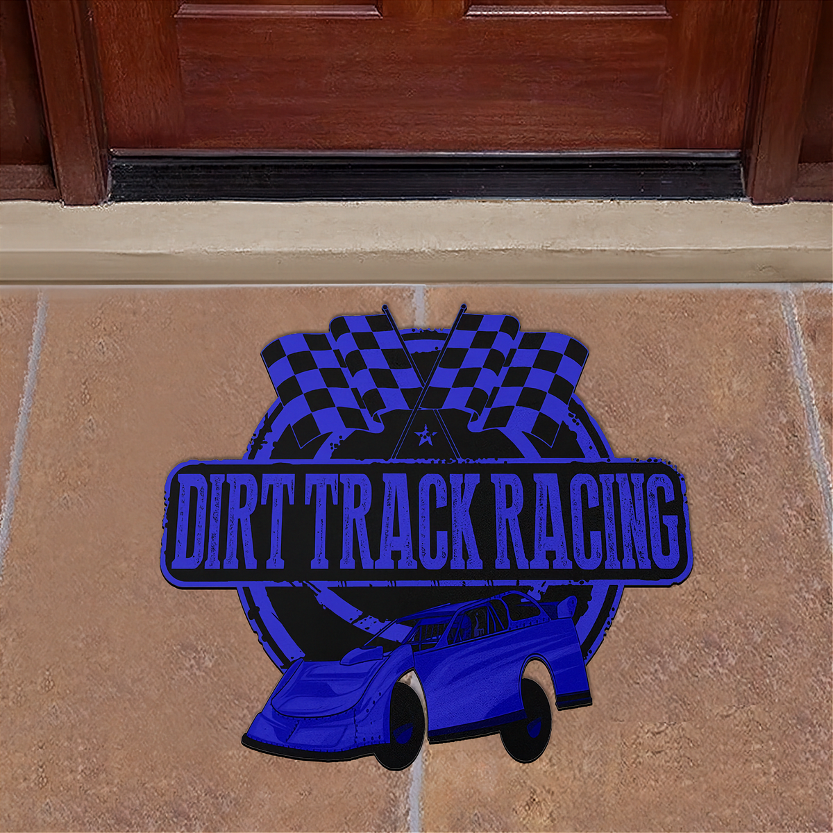 A die-cut vinyl doormat featuring a blue and black 'Dirt Track Racing' design with a race car and checkered flags, displayed on a tan stone tile floor in front of a dark wood door.