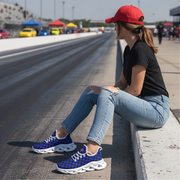 Woman sitting on a race track wearing blue sneakers with white soles, black shirt, and red cap.