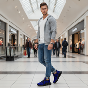 Man in a gray hoodie and blue jeans  and checkered blue shoes standing in a shopping mall.