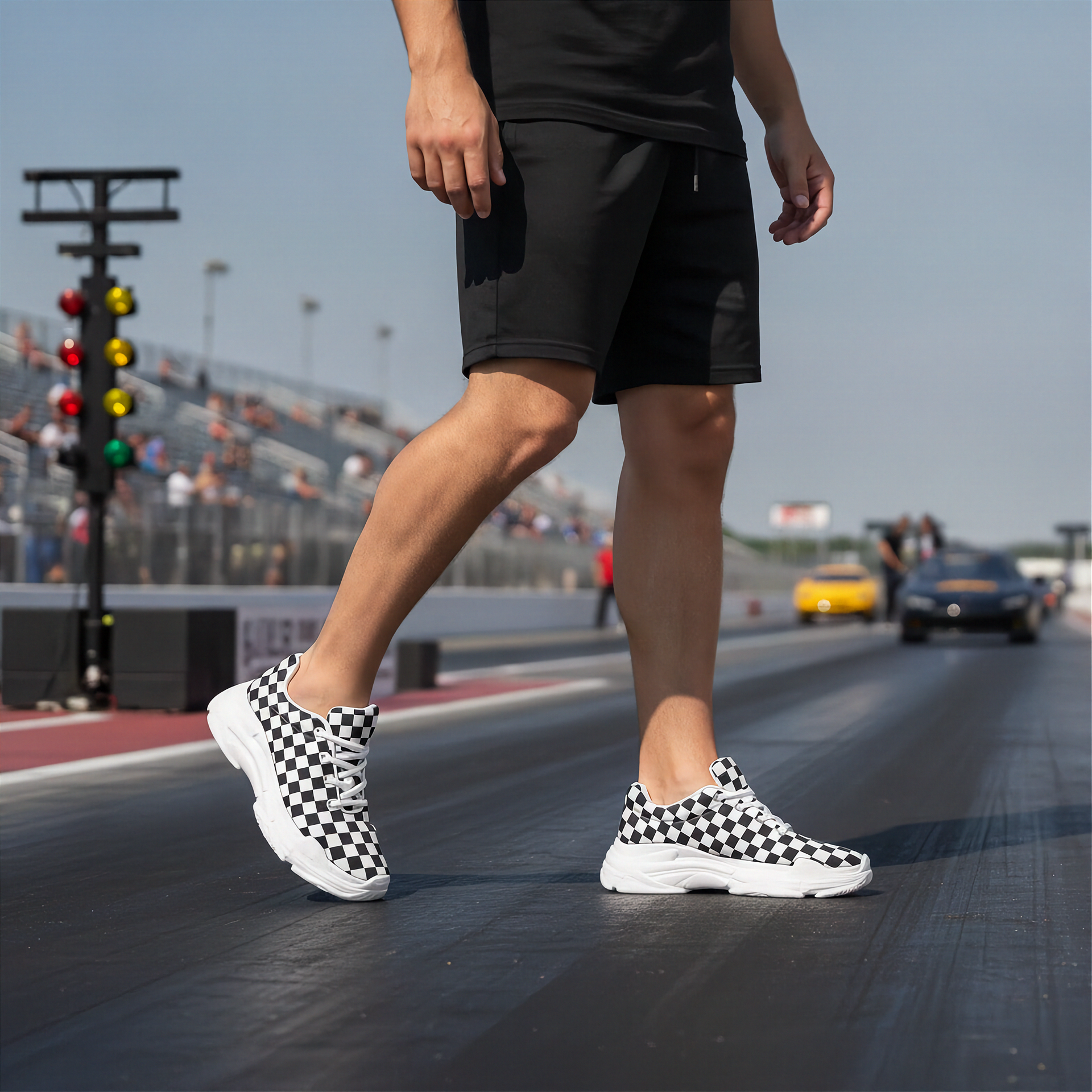 Man wearing black checkered sneakers on a racetrack with cars and traffic lights in the background.