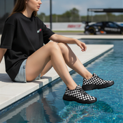 Woman wearing black and white checkered shoes sitting by a pool.