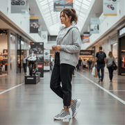 Woman standing in a shopping mall wearing a gray hoodie and black pants with checkered shoes.