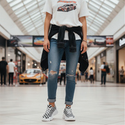 Woman wearing a graphic t-shirt, ripped jeans, and checkered shoes in a mall setting.