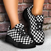 Black and white checkered sneakers worn by a person standing against a brick wall.