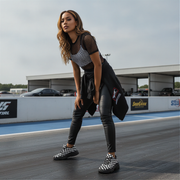 Woman in checkered top and leather pants standing on a race track with racing-themed background