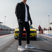Man wearing checkered shoes standing on a race track with a colorful car in the background
