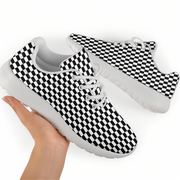 Hand holding a black-and-white checkered sneaker with white laces and sole, with the matching shoe behind it.