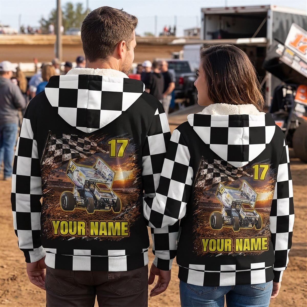 Couple wearing matching personalized sprint car sherpa jackets at a dirt track, showing checkered backs with car, name, and number.