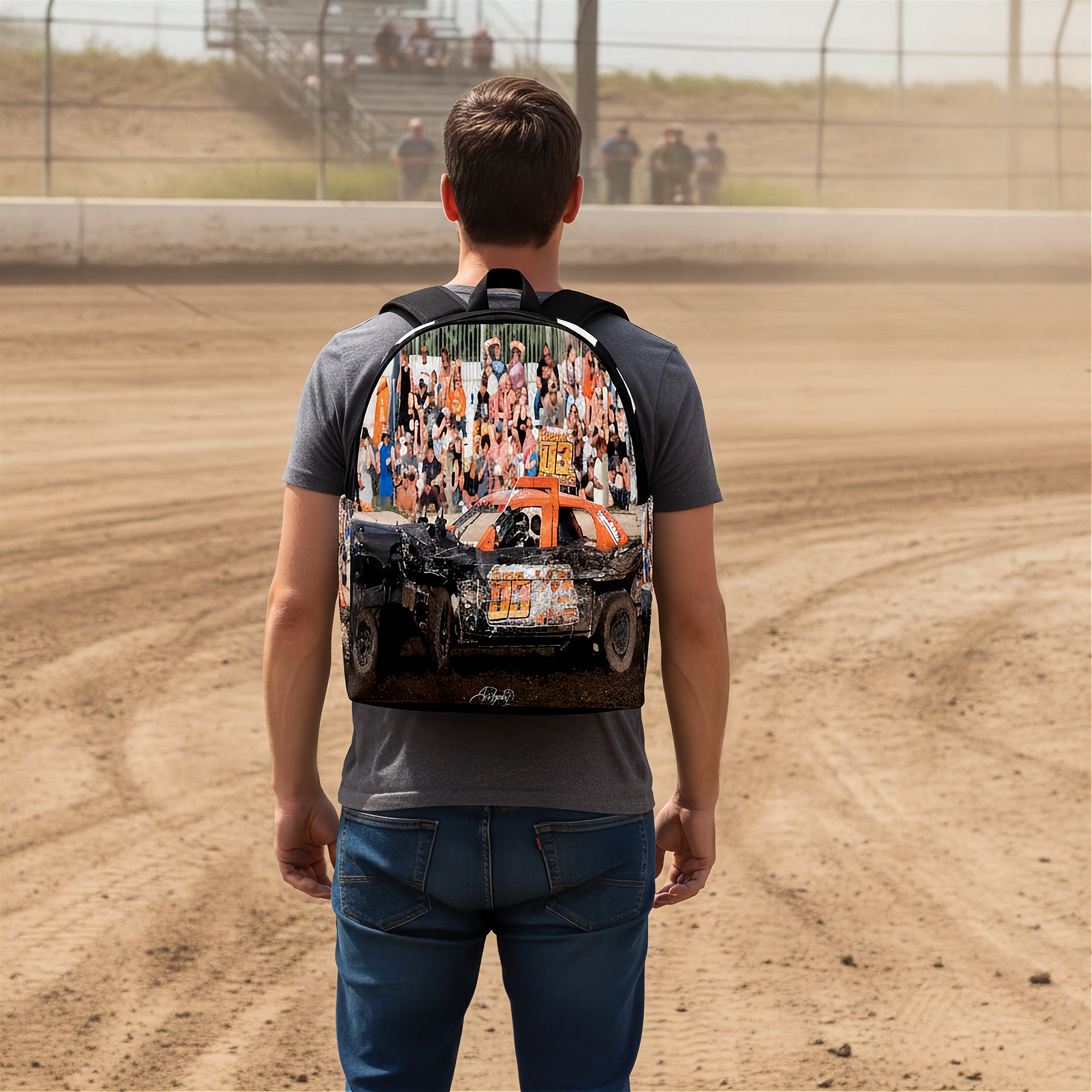 A man viewed from behind wearing a gray t-shirt and blue jeans, carrying a backpack on his back. The backpack features a graphic print of an orange and white Demolition derby car with a crowd of spectators in the background.