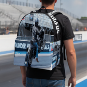 A person viewed from behind wearing a custom-printed drag racing backpack with a motorcycle racer graphic and 'HULIFAS' printed on the side, set against a racetrack background.