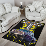 A rectangular area rug with a graphic design of a purple classic race car and the words 'PRESTAGE RACE NIGHT' on a black background, shown in a living room setting between two white armchairs.