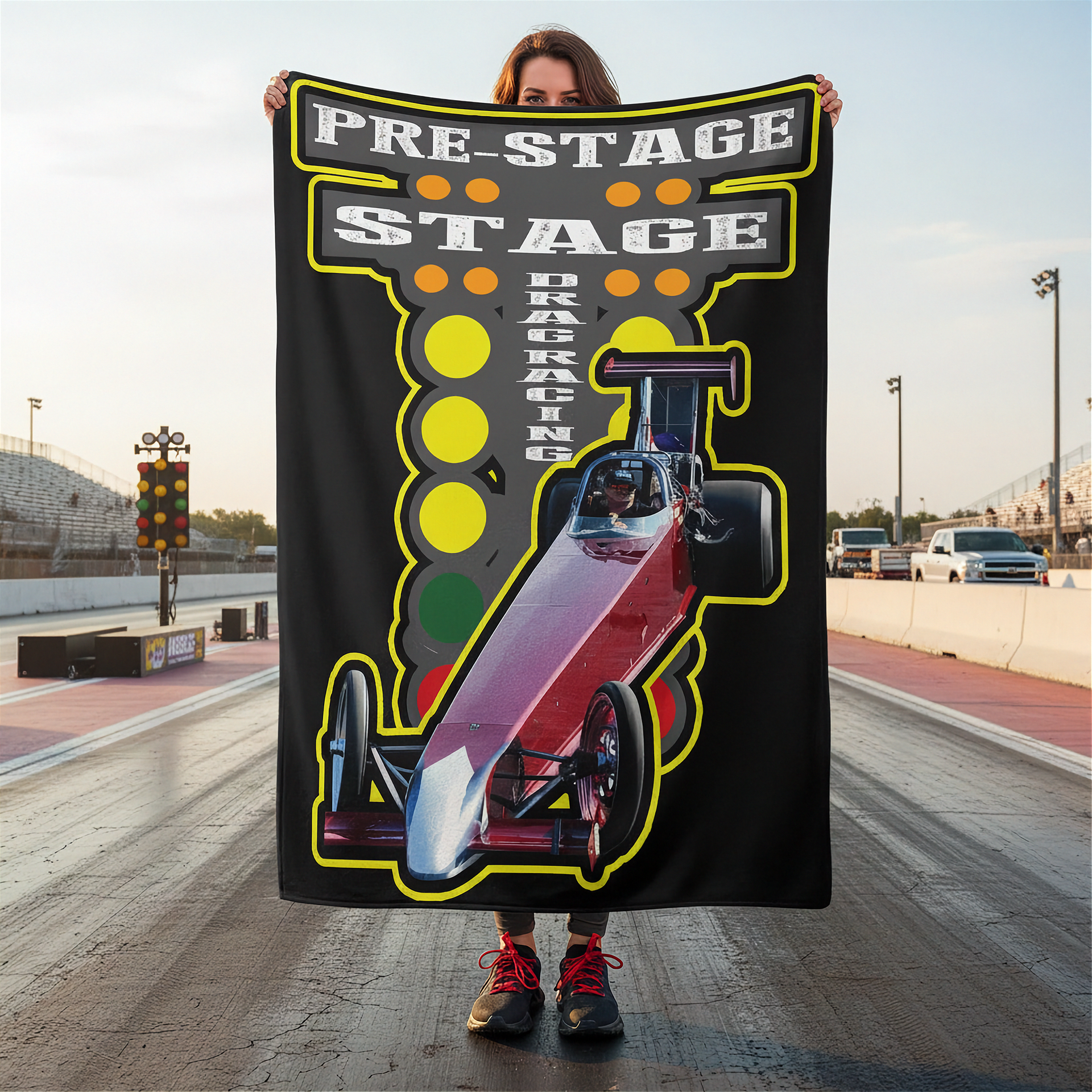 Person holding a 'Pre-Stage Stage Parking' blanket with a race car design on a race track.