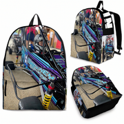 A backpack shown from multiple angles on a plain white background, printed with a detailed race car scene. The backpack has black straps and trim, and the printed artwork features a blue, purple, black, and tan race car with bright yellow suspension and racing graphics.