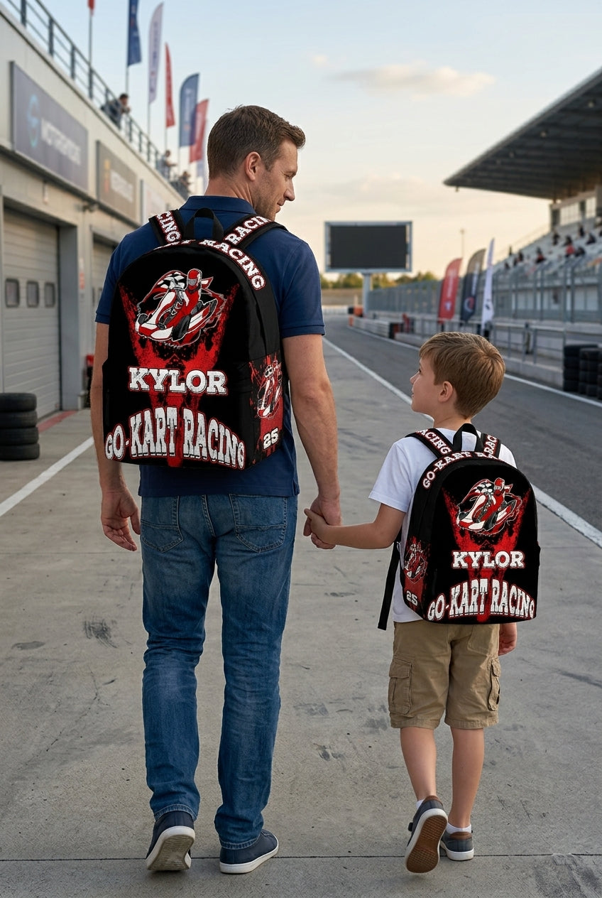 An adult man and an 8 to 12 year old child walking hand-in-hand down a professional outdoor go-kart track pit lane, both wearing matching custom Kaylor N25 kart racing backpacks viewed from behind.