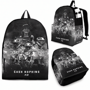 A black backpack shown from multiple angles on a white background, featuring a grayscale motocross graphic with the text 'CASH HOPKINS #10' and a portrait of a woman. No visible brand logo is present.