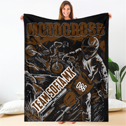 Woman holding a brown and black personalized motocross blanket with sample team name and number 086 indoors.