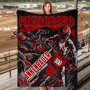 Woman holding a red and black personalized motocross blanket with sample name and number 500 in trackside bleachers.