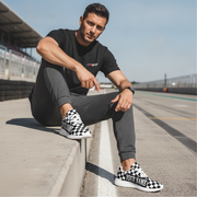 Man sitting on a race track wearing black and white checkered sneakers with 'Your Name' text.