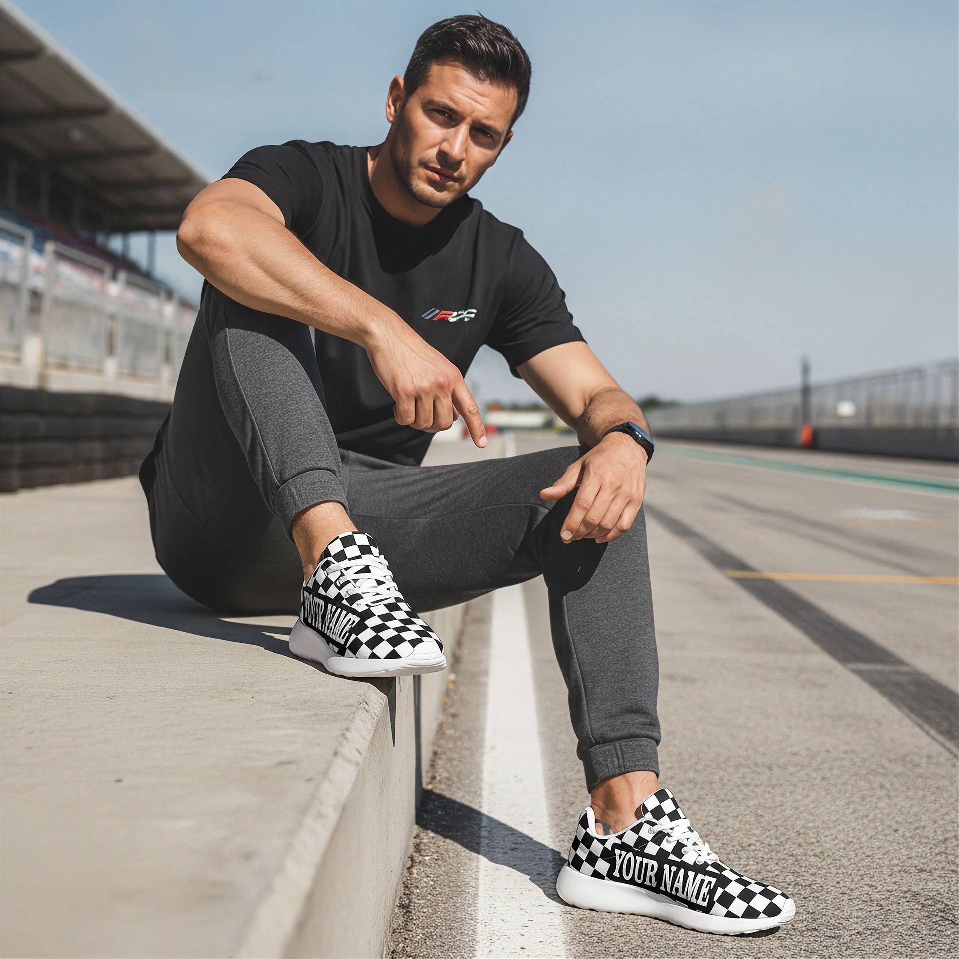 Man sitting on a race track wearing black and white checkered sneakers with 'Your Name' text.