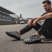 Man sitting on a race track wearing black and white checkered shoes with 'CINDY' branding.