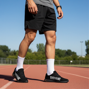 Person wearing black athletic shoes with 'YOUR NAME' printed on them, standing on a track.