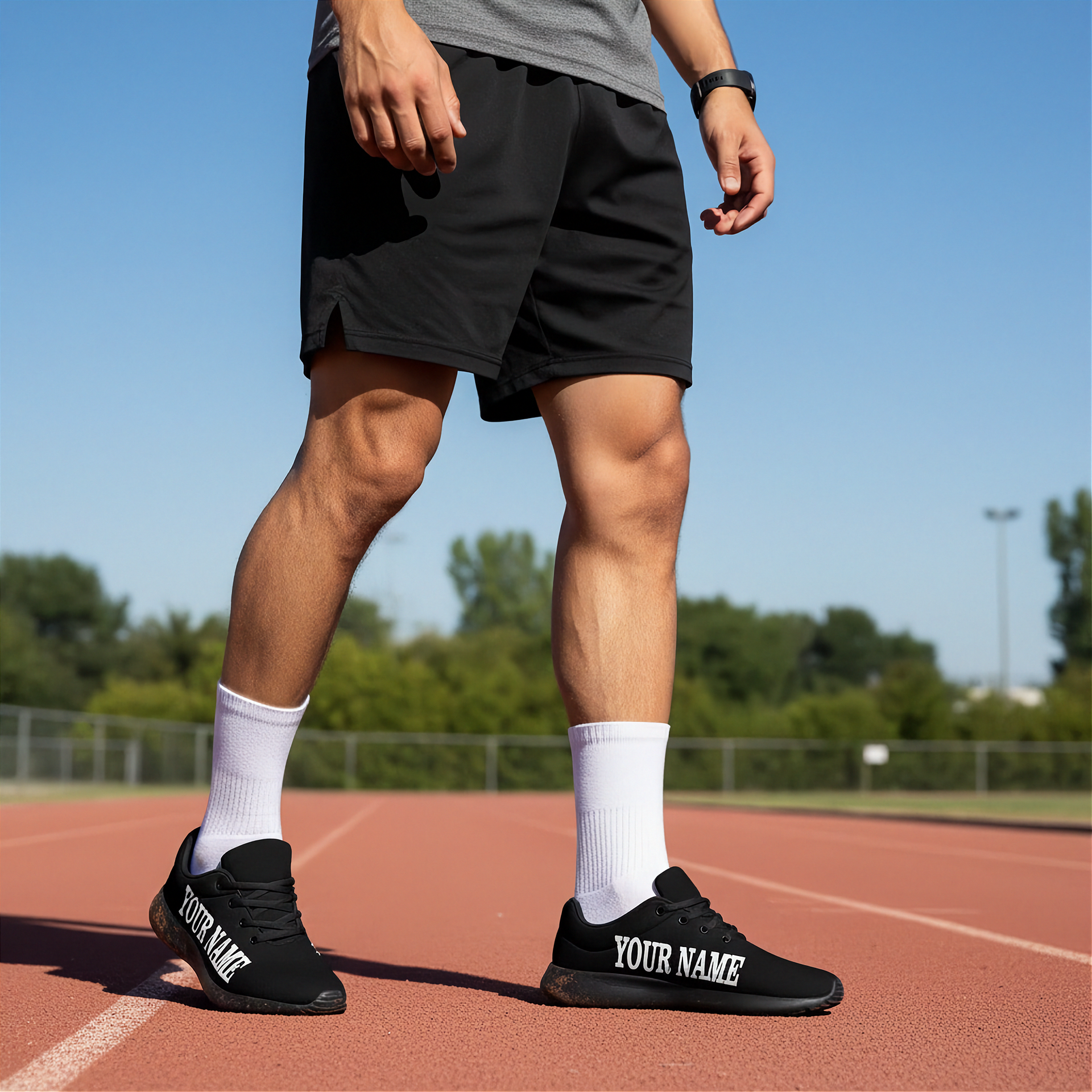 Person wearing black athletic shoes with 'YOUR NAME' printed on them, standing on a track.
