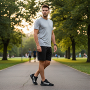 Man walking on a path in a park wearing a gray t-shirt, black shorts, and black sneakers.