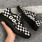 Black and white checkered sneakers with a hand holding one shoe on a concrete surface.