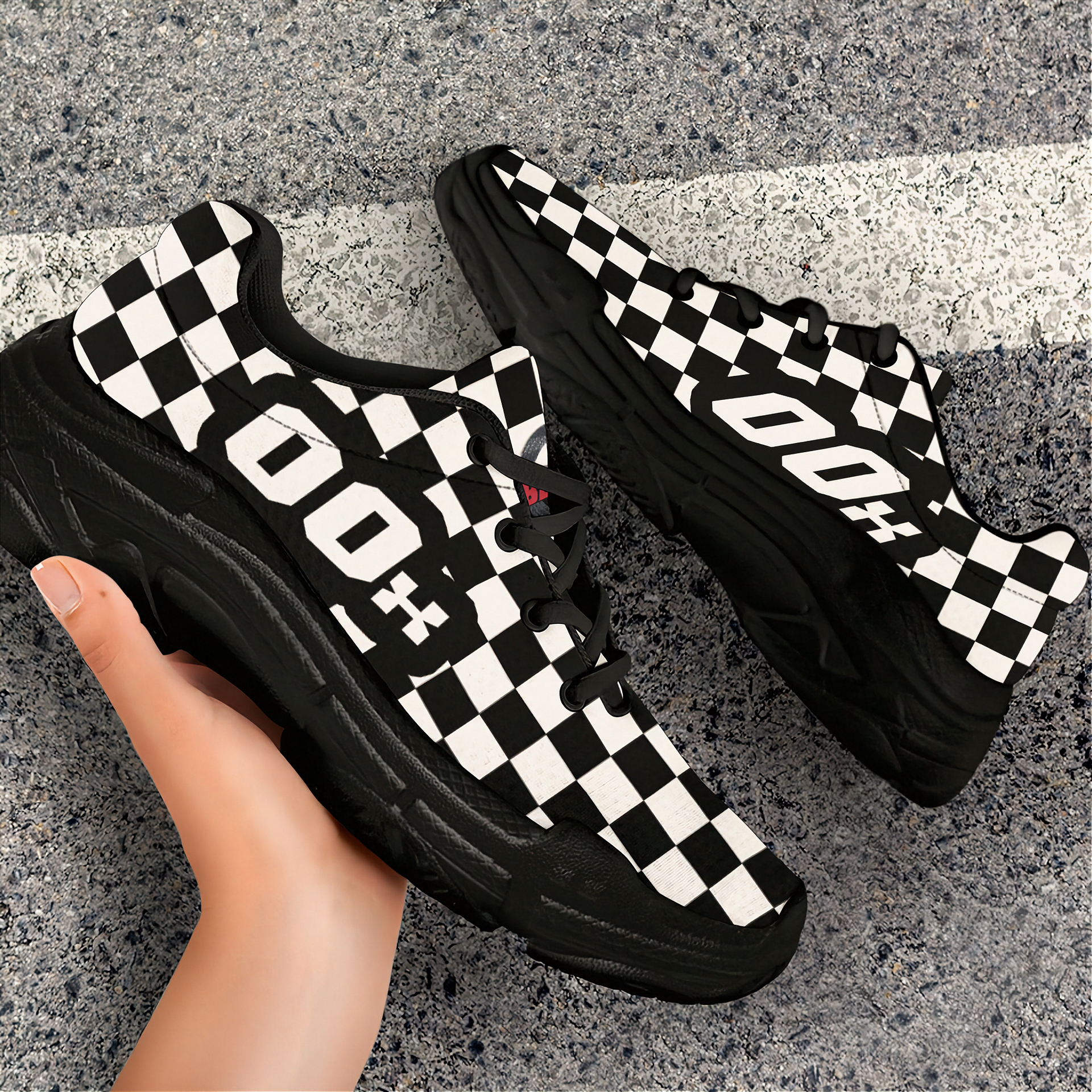 Black and white checkered sneakers with a hand holding one shoe on a concrete surface.