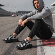 Man sitting on a race track wearing checkered shoes and a gray hoodie.