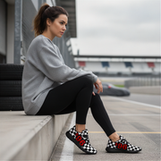 Woman sitting on a concrete ledge wearing checkered shoes with numbers, in an outdoor setting.