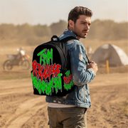 A man wearing a black backpack with a large colorful graffiti-style graphic reading 'THAT'S RICKLES REDEMPTION' stands in a dusty outdoor desert-like setting with a dirt bike and tent in the background.