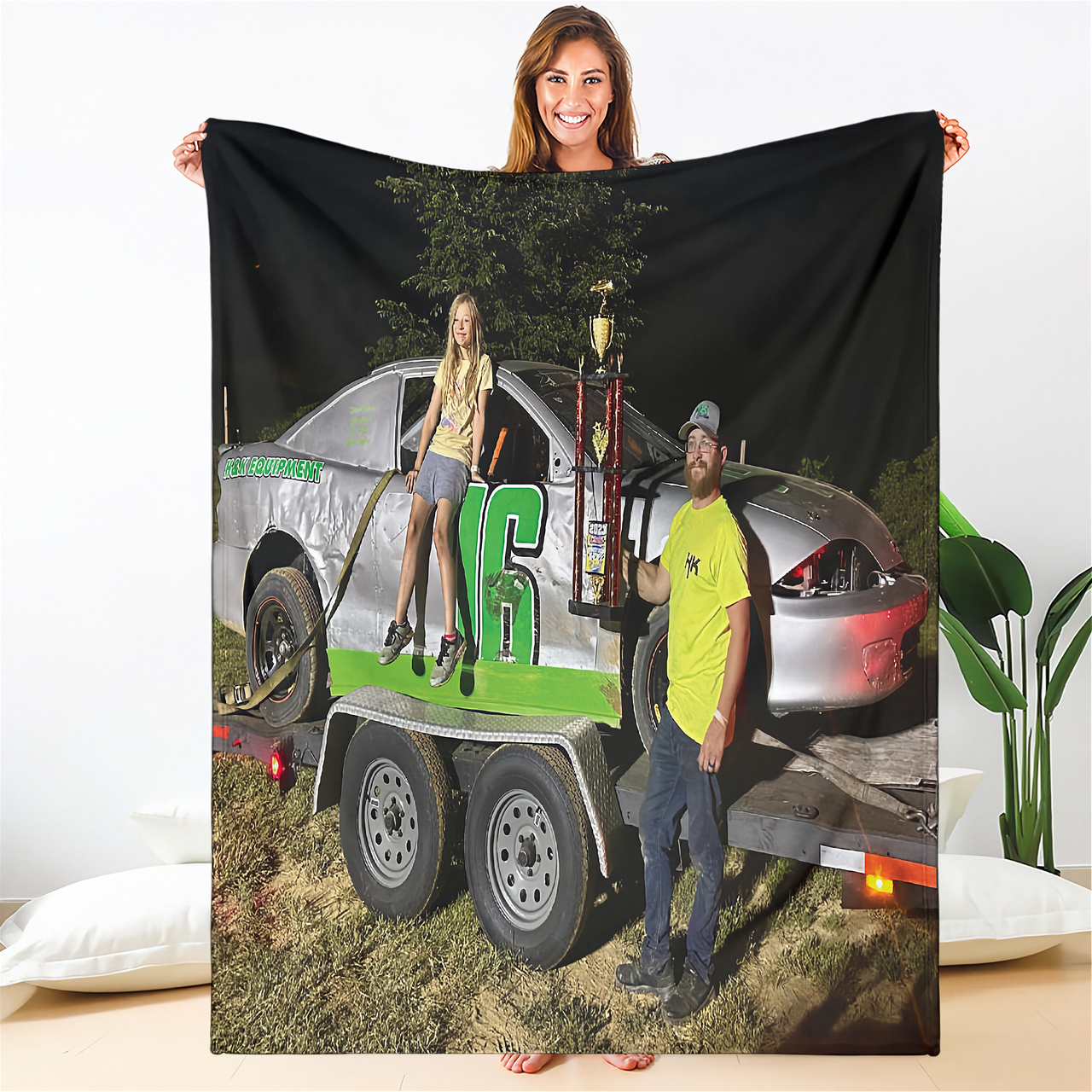 Woman holding a blanket with a printed image of a man and woman by a truck.