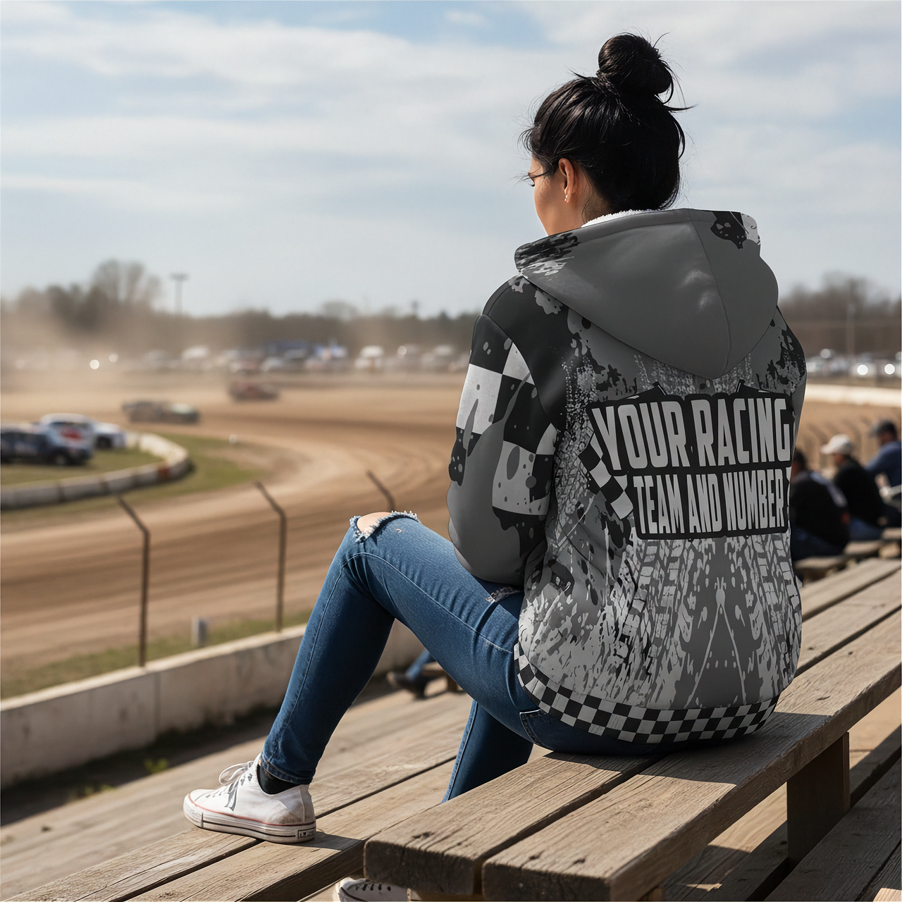 Person sitting on a wooden bench at a race track, wearing a custom sherpa hoodie with on a dirt track