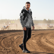 Man in a patterned racing sherpa jacket standing on a dirt track with motocross bikes in the background.