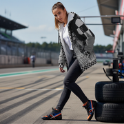 Woman walking on a race track with tires in the background wearing a custom racing sherpa jacket