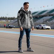 Man standing on a race track wearing a custom checkered patterned sherpa jacket and jeans, with a car in the background.