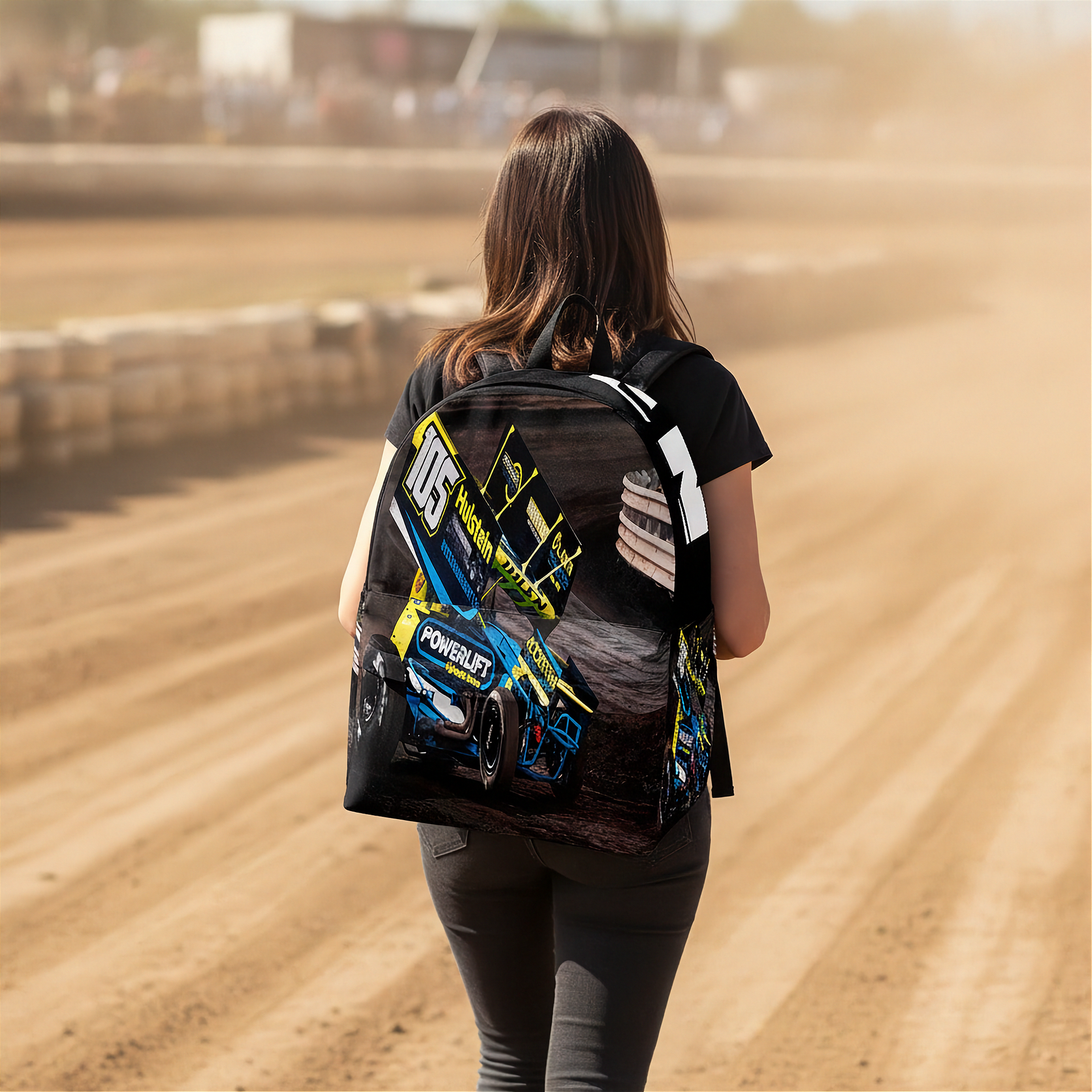 A woman seen from behind walking on a dirt racetrack wearing a black backpack with a large graphic print of a blue and yellow sprint race car and the number 115.