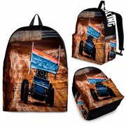 A backpack shown from multiple angles on a white background, featuring a printed racing scene with a blue sprint car and a blue, orange, and red flag. The backpack itself is black with white text on the shoulder strap.