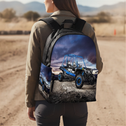 A woman on a race track wearing a custom UTV Buggy backpack with a printed graphic of race cars and the word 'UTV Buggy' on the strap, viewed from behind.