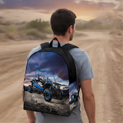 A man viewed from behind wearing a black backpack with a full-color graphic print of a buggy standing on an outdoor dirt race track
