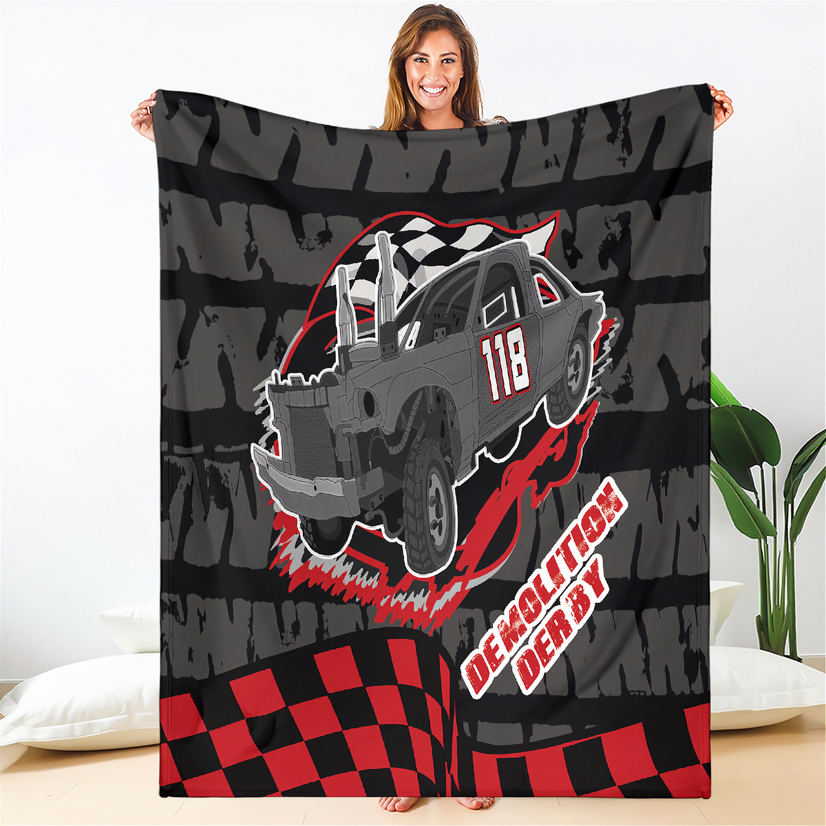 Woman holding a custom demolition derby blanket featuring a gray number 118 car, red accents, and a dark tire-track background.