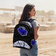 A woman standing in a dusty outdoor setting wearing a black backpack with a blue car graphic and 'Demolition Derby' text printed on it.