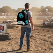 A man viewed from behind standing on a dirt racetrack wearing a black backpack with a large blue and white demolition derby graphic on the back and a smaller matching graphic on the side. Racing cars and a crowd are visible in the background.
