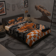 A bed dressed in a racing-themed bedding set with orange, black, and white graphics, including a checkered blanket corner and matching pillowcases, shown in a styled bedroom with car wall art and racing decor.